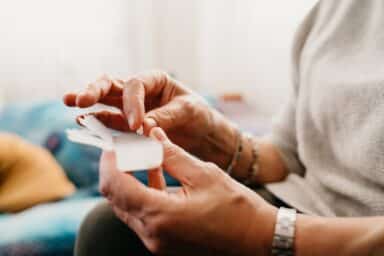 A woman's hands reach for her bipolar disorder medication from a clear plastic box.