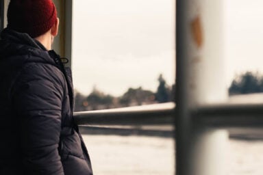 A lone man in a black jacket and red beanie stares out of a window at an empty cityscape, reflecting the detached nature of cluster A personality disorders.